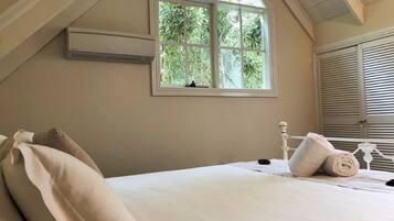 A bedroom with a large window, a bed with pillows, a bedside table, and a lamp.