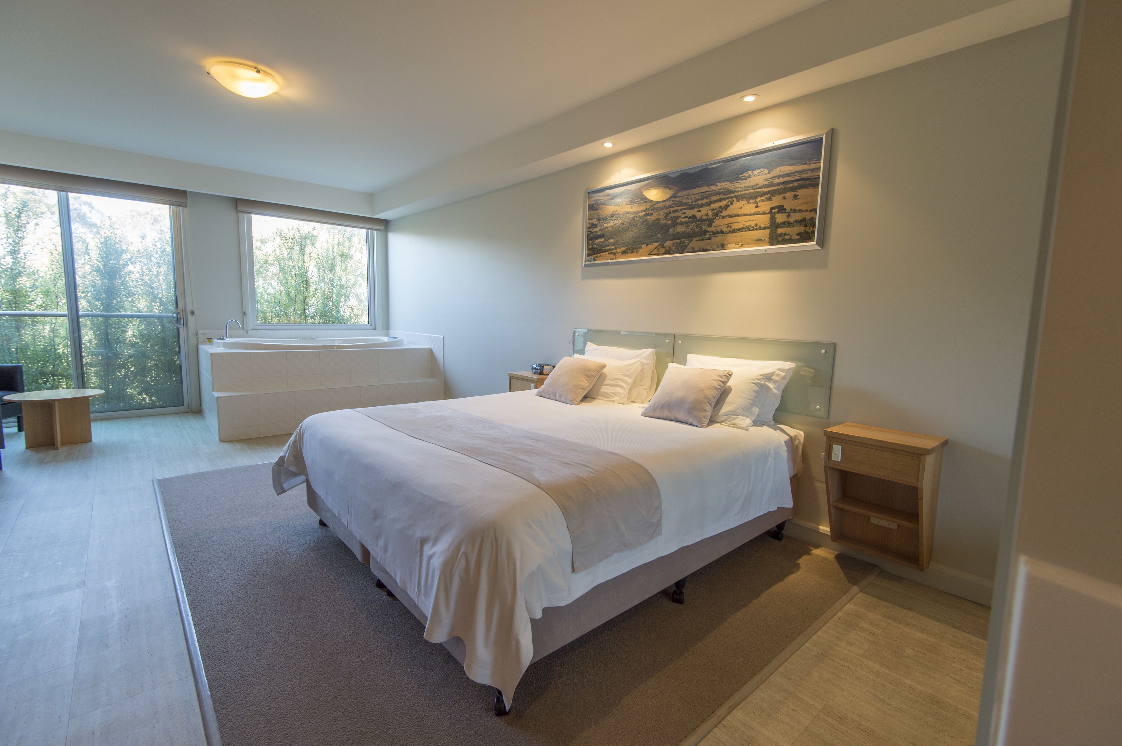 A modern bedroom with a large bed, bedside tables, a window with a view, and a painting on the wall.