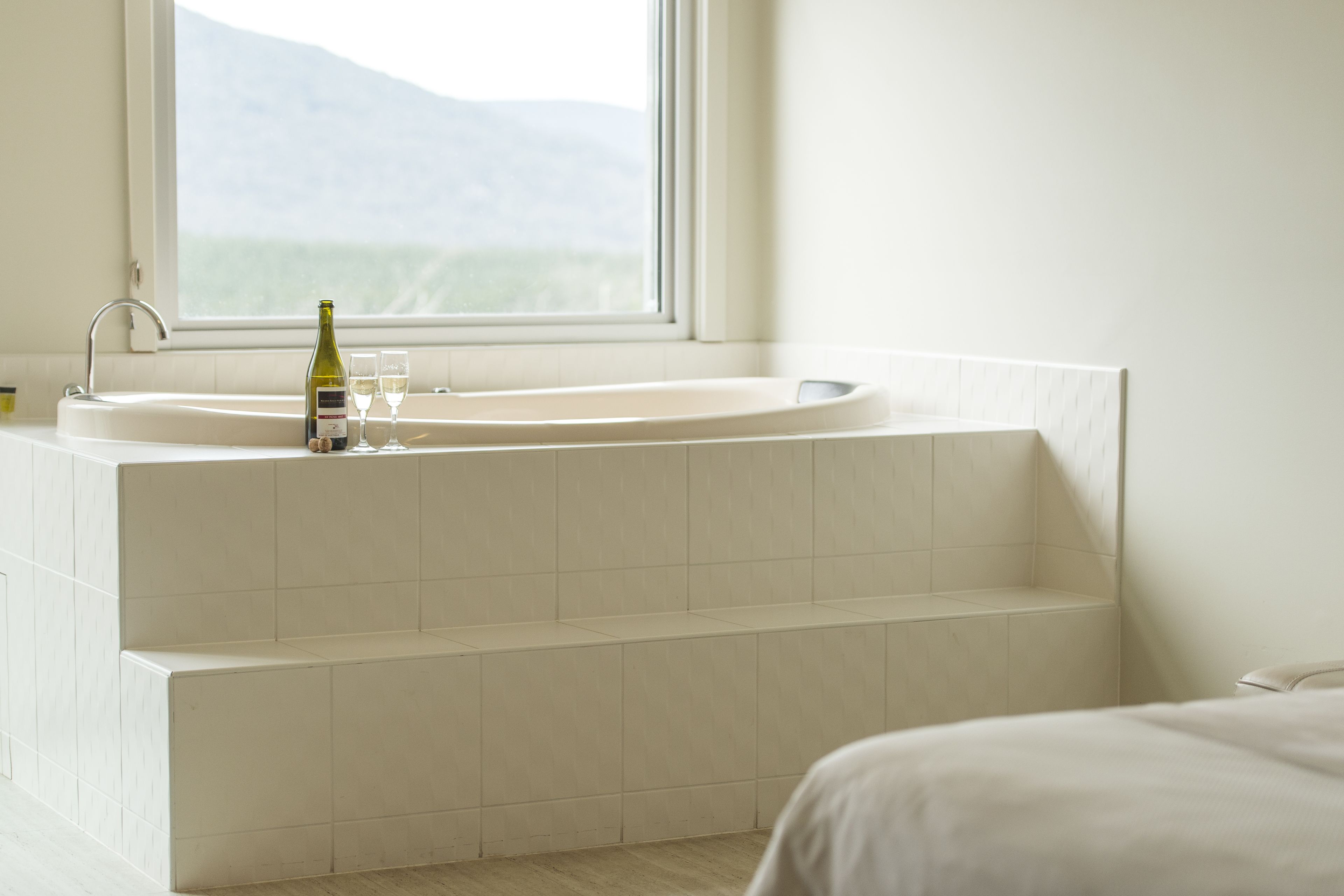 A bathroom with a large bathtub, a window with a view of mountains, and a bottle of wine on the sink.