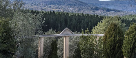 A stone gazebo with columns, surrounded by trees and a mountain in the background.