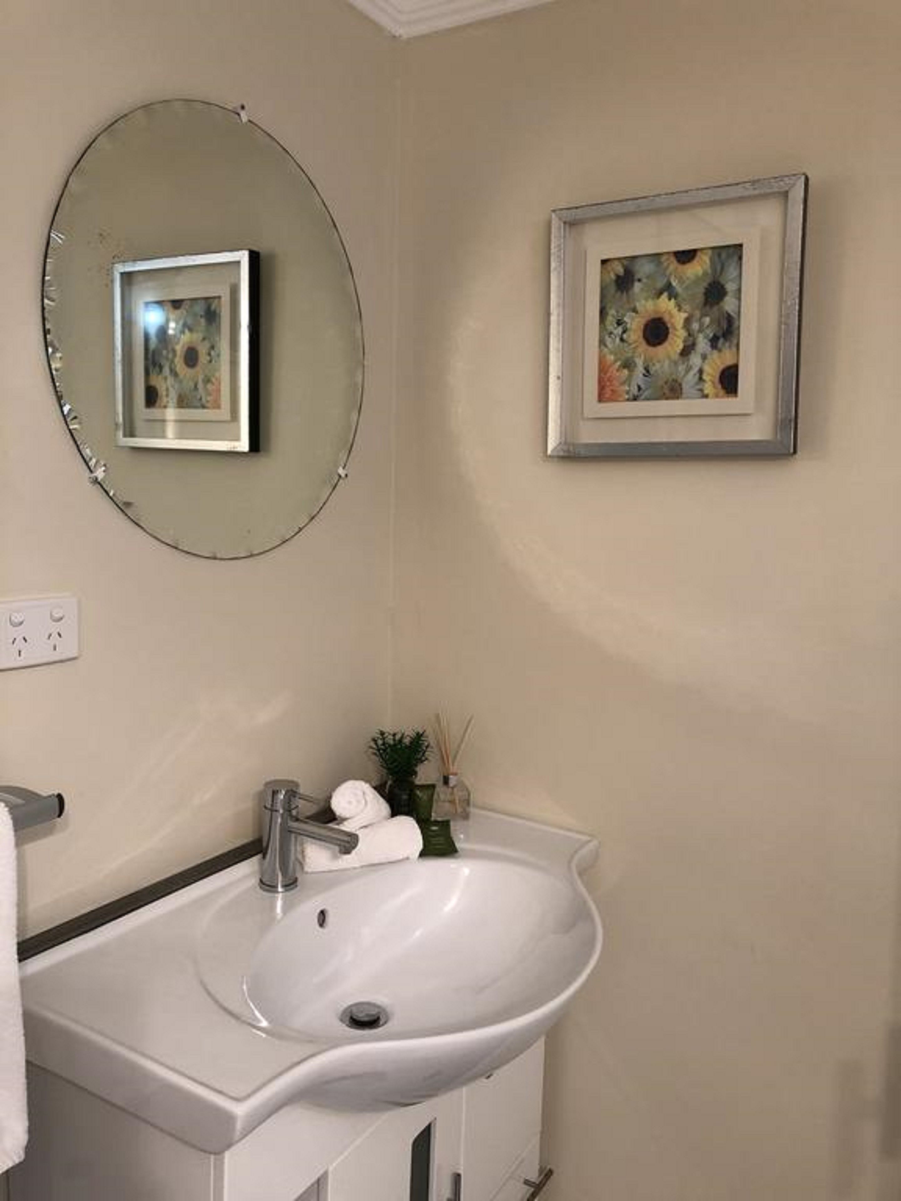 A bathroom with a white sink, a round mirror, and a framed painting on the wall.
