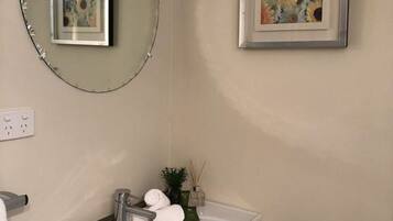 A bathroom with a white sink, a round mirror, and a framed painting on the wall.