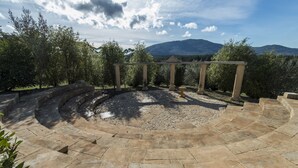 Un anfiteatro al aire libre con escalones y columnas de piedra, rodeado de árboles y un paisaje montañoso.