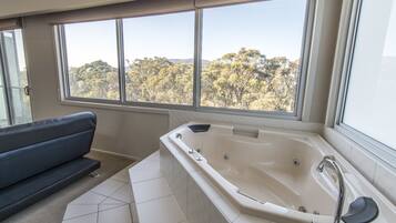 Un baño moderno con una bañera grande, un sofá y vistas a un bosque a través de amplios ventanales.