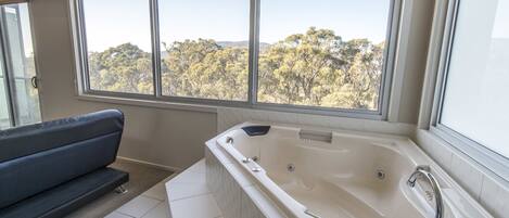 Un baño moderno con una bañera grande, un sofá y vistas a un bosque a través de amplios ventanales.