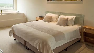 A neatly made bed with a headboard, a bedside table with a lamp, and a window with a view of greenery.