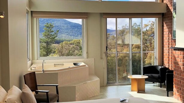 Un dormitorio moderno con una cama grande, una zona de estar, una bañera y vistas al exterior.