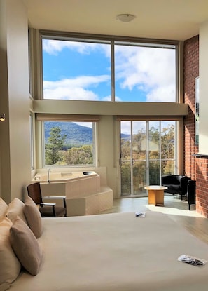 A modern bedroom with a large bed, a seating area, a bathtub, and a view of the outdoors. - Macedon Ranges Hotel & Spa (Macedon)