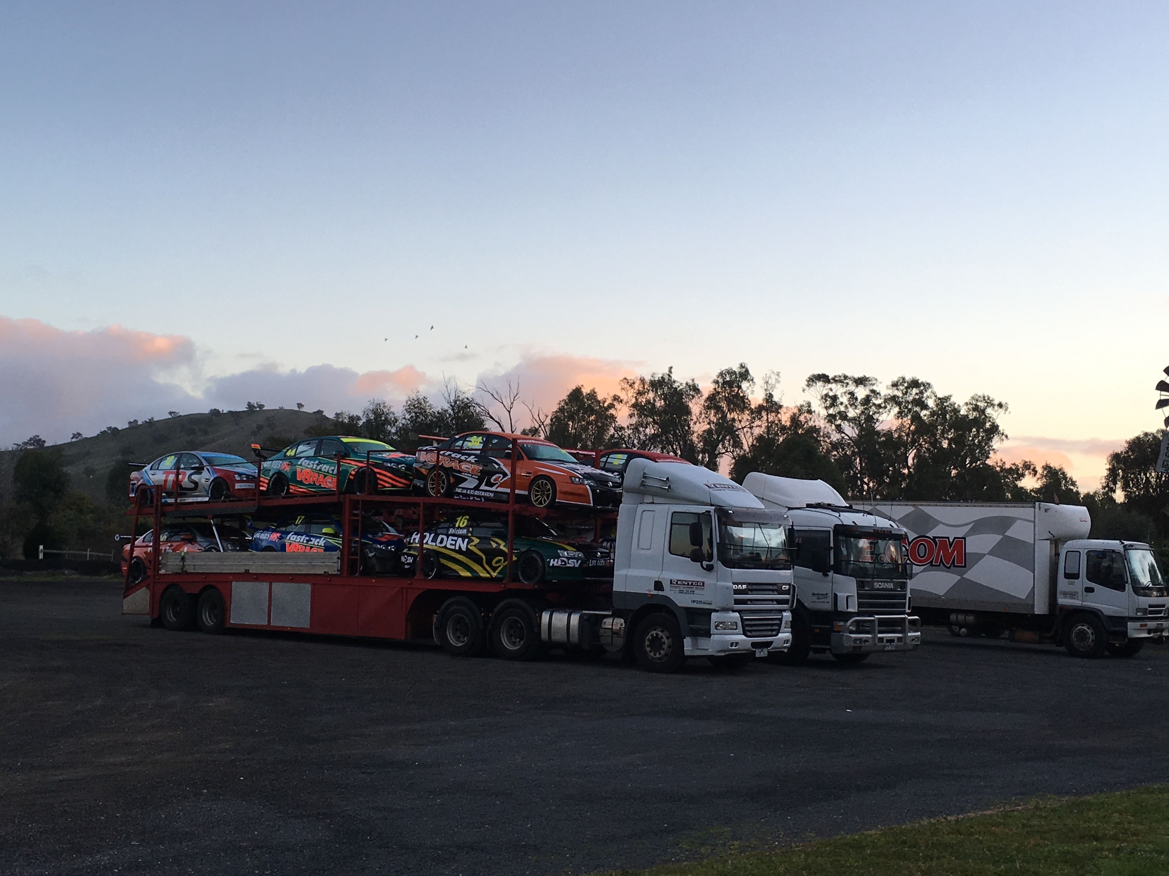 A large truck with multiple cars on its bed, parked in a lot with a hilly background.