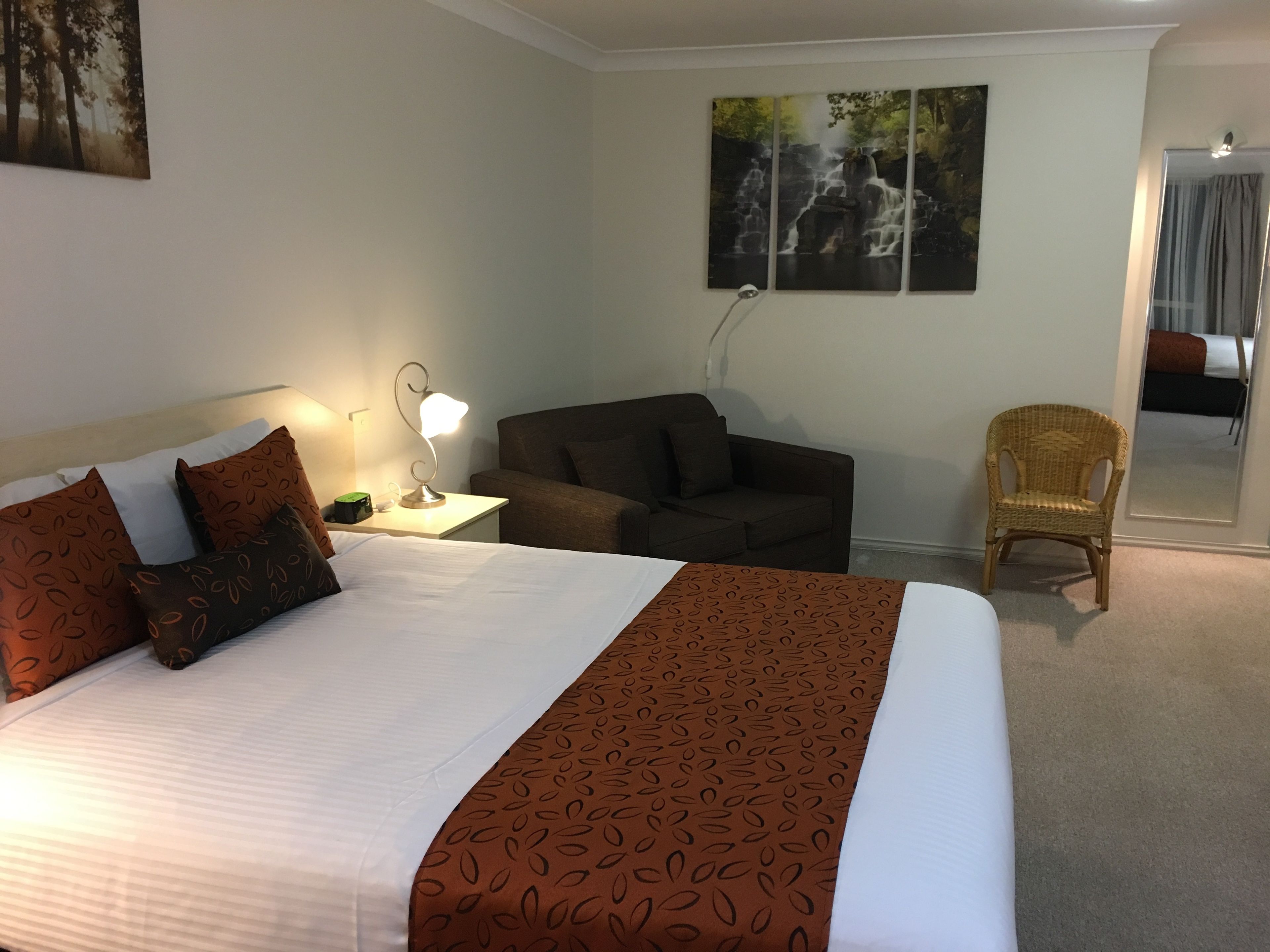 Una habitación de hotel con una cama grande, un escritorio con lámpara, un sofá y una silla. Hay dos cuadros en la pared.