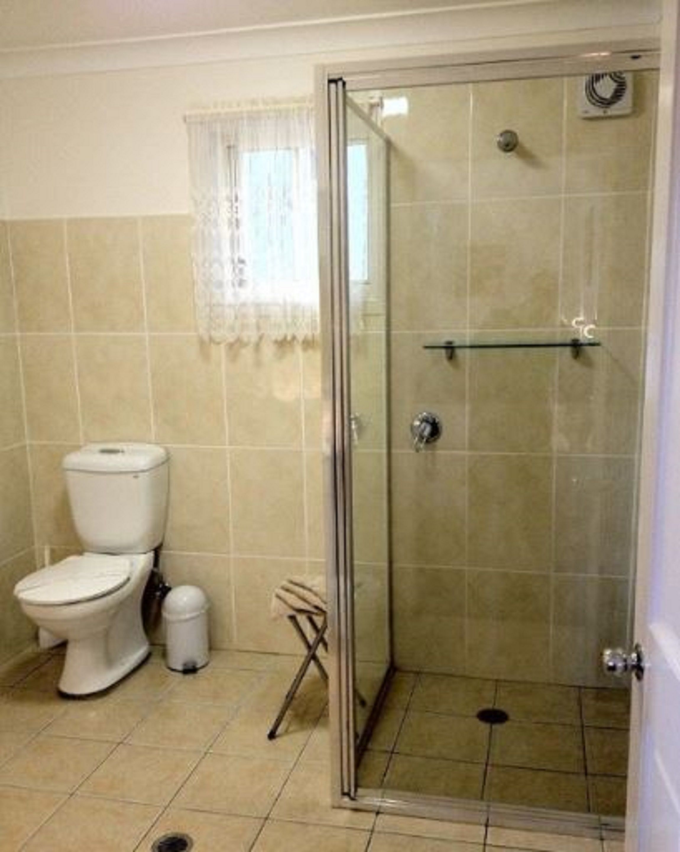 A bathroom with a toilet, a glass-enclosed shower, and a tiled floor.