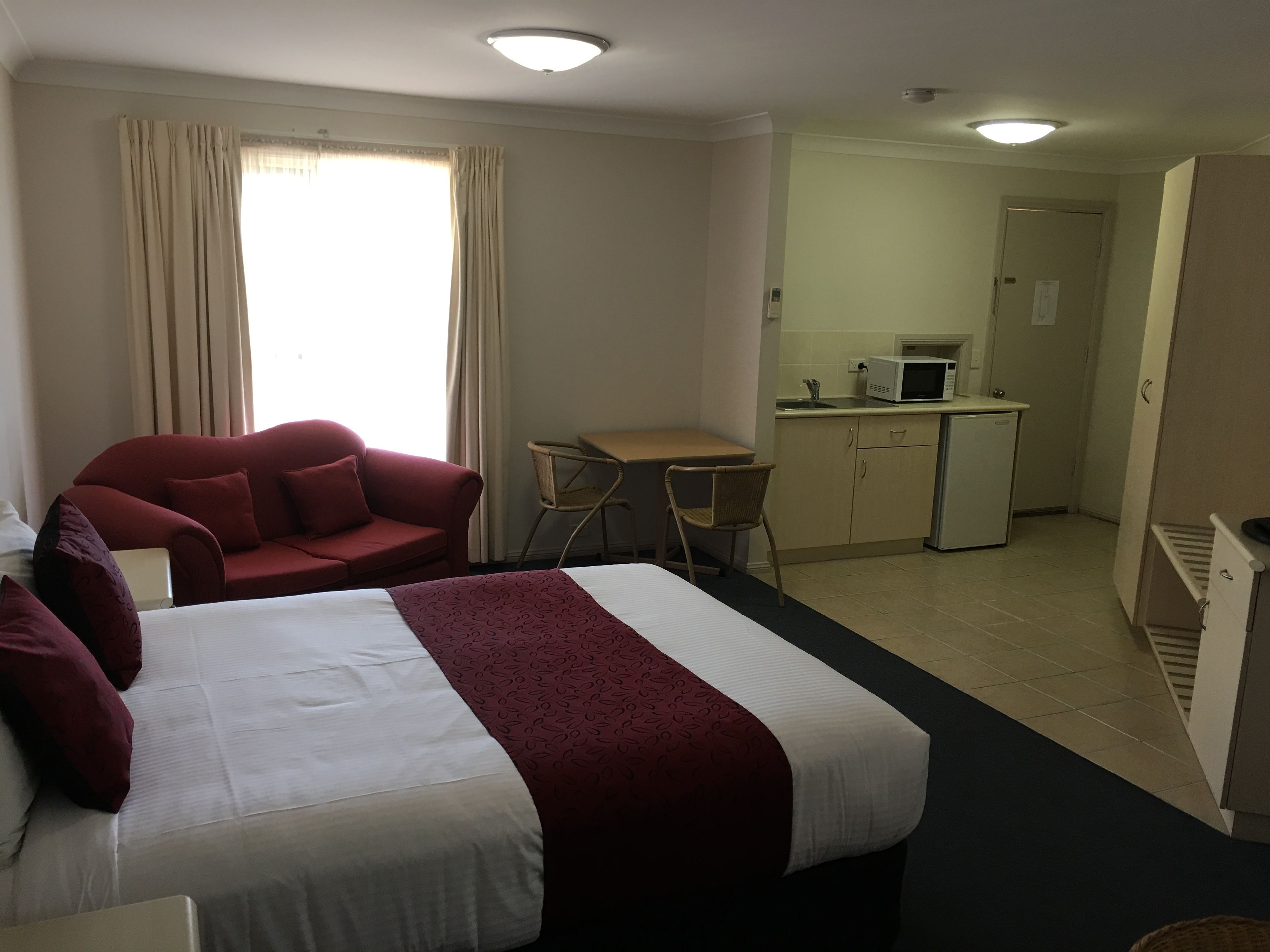 Een hotelkamer met een bed, een rode fauteuil, een tafeltje en een kitchenette.