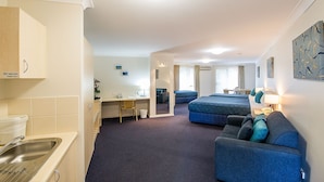 A hotel room with a kitchenette, a desk, two beds, and a seating area. - Tuckerbox Motor Inn (South Gundagai)