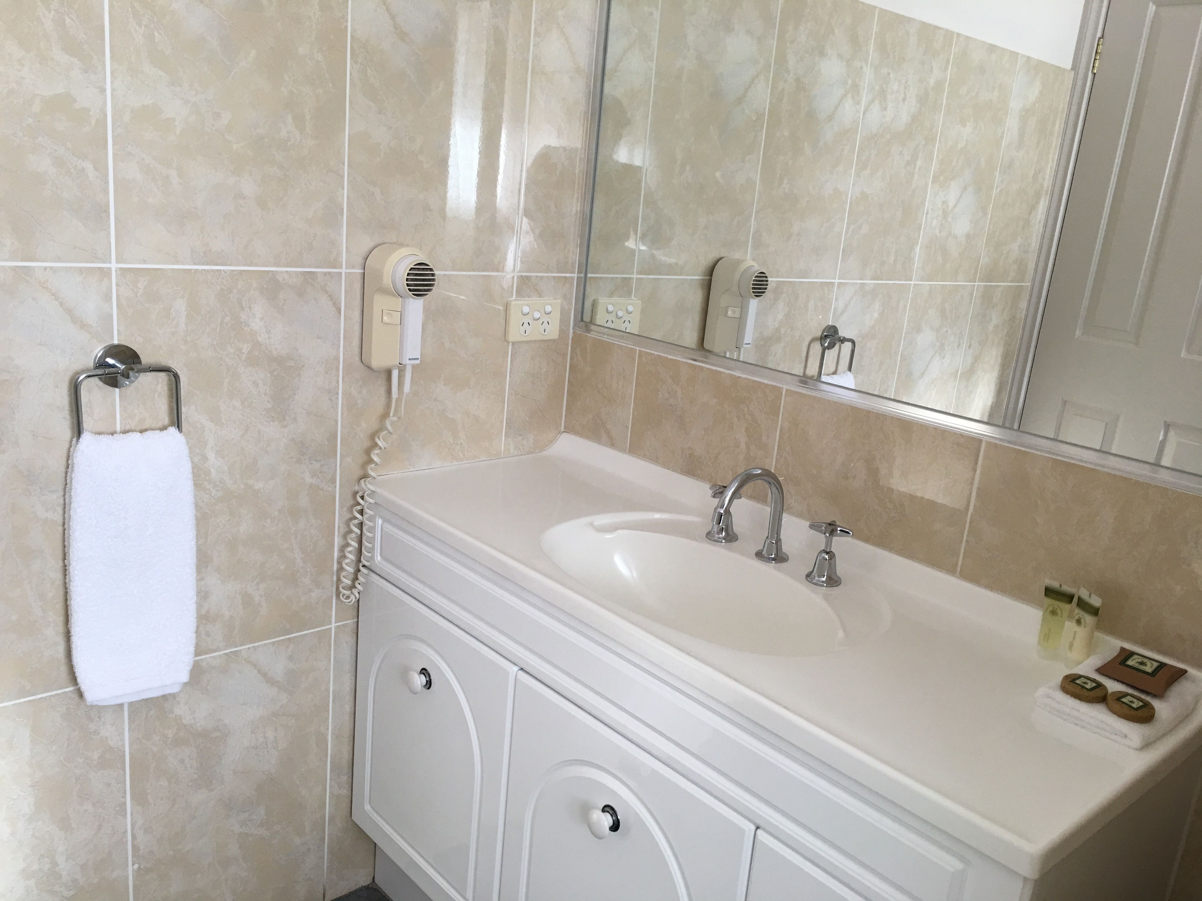 A bathroom with a white sink, two faucets, a towel rack with a white towel, a mirror, and a small bottle of soap on the counter.