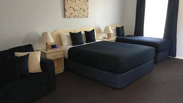Une chambre d’hôtel avec deux lits, un canapé, une table de chevet, une lampe et une fenêtre avec des rideaux.