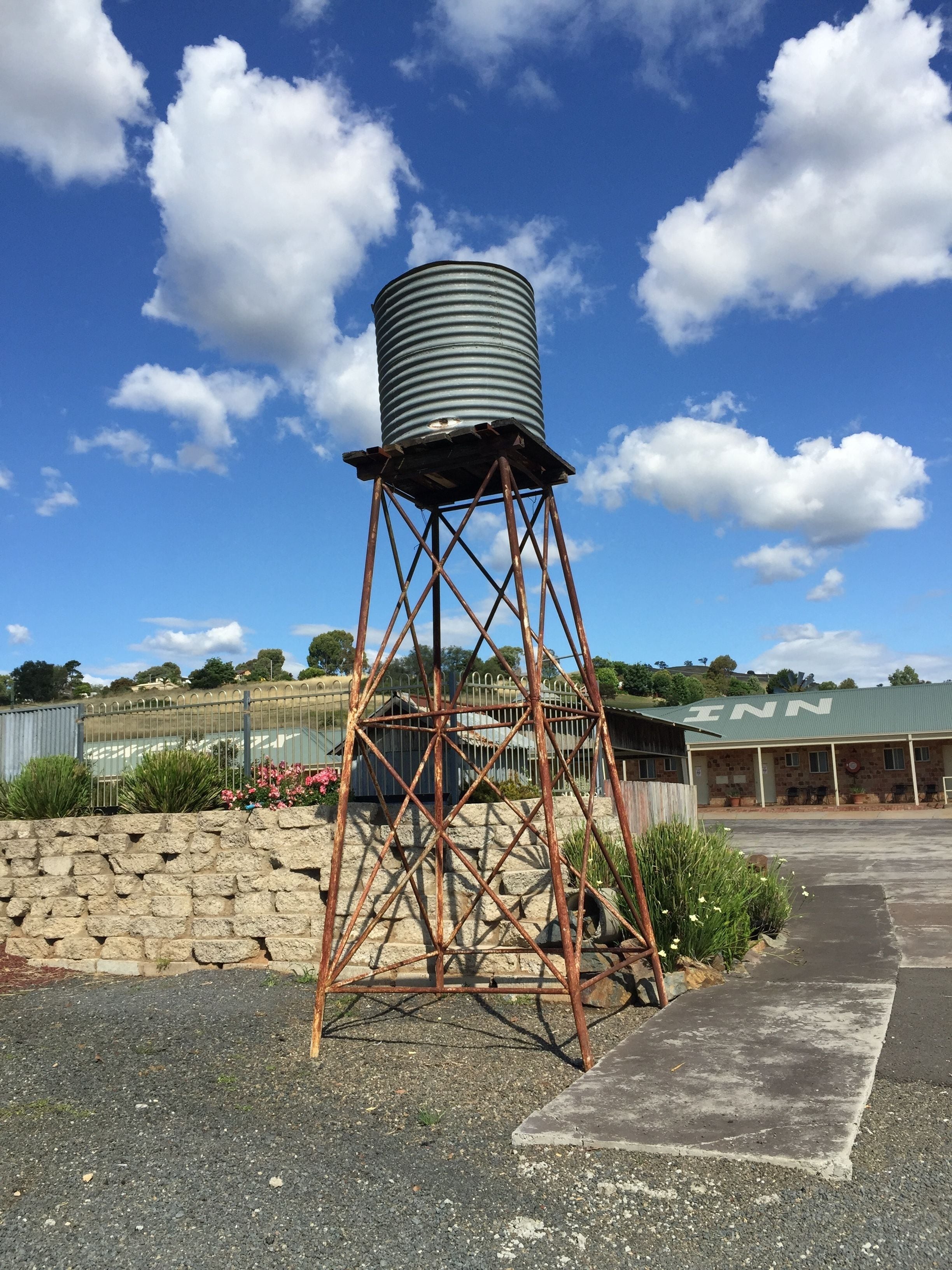Vandtårn med metalkonstruktion og en cylindrisk tank øverst, mod en klar blå himmel med skyer.