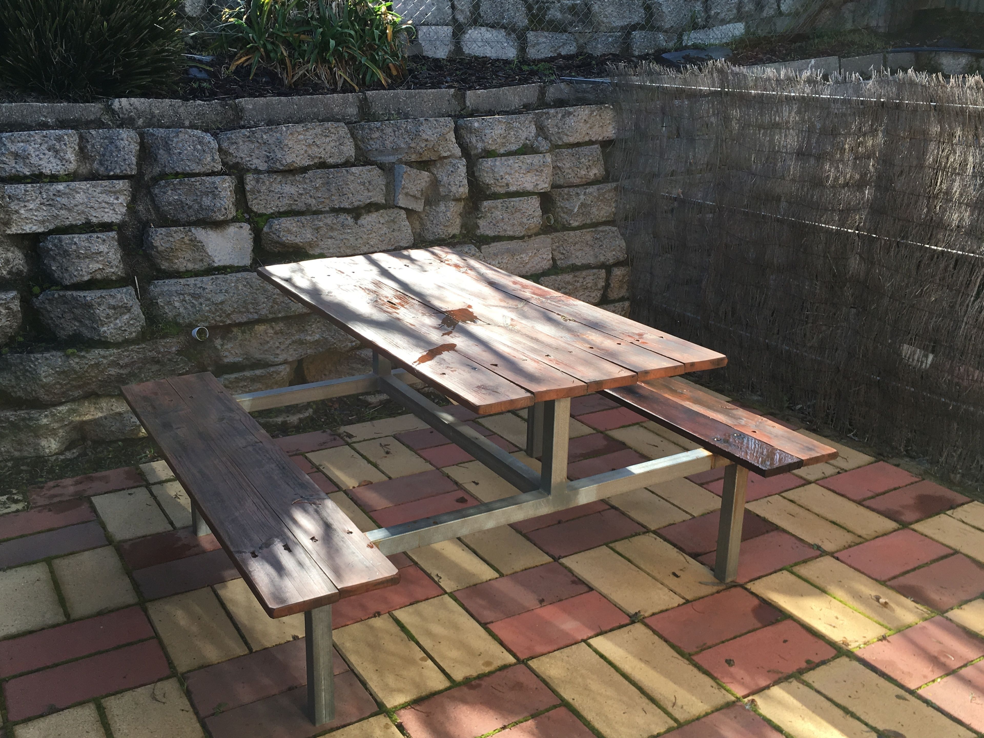 Una mesa de picnic con bancos, frente a una pared de piedra y suelo de ladrillo.