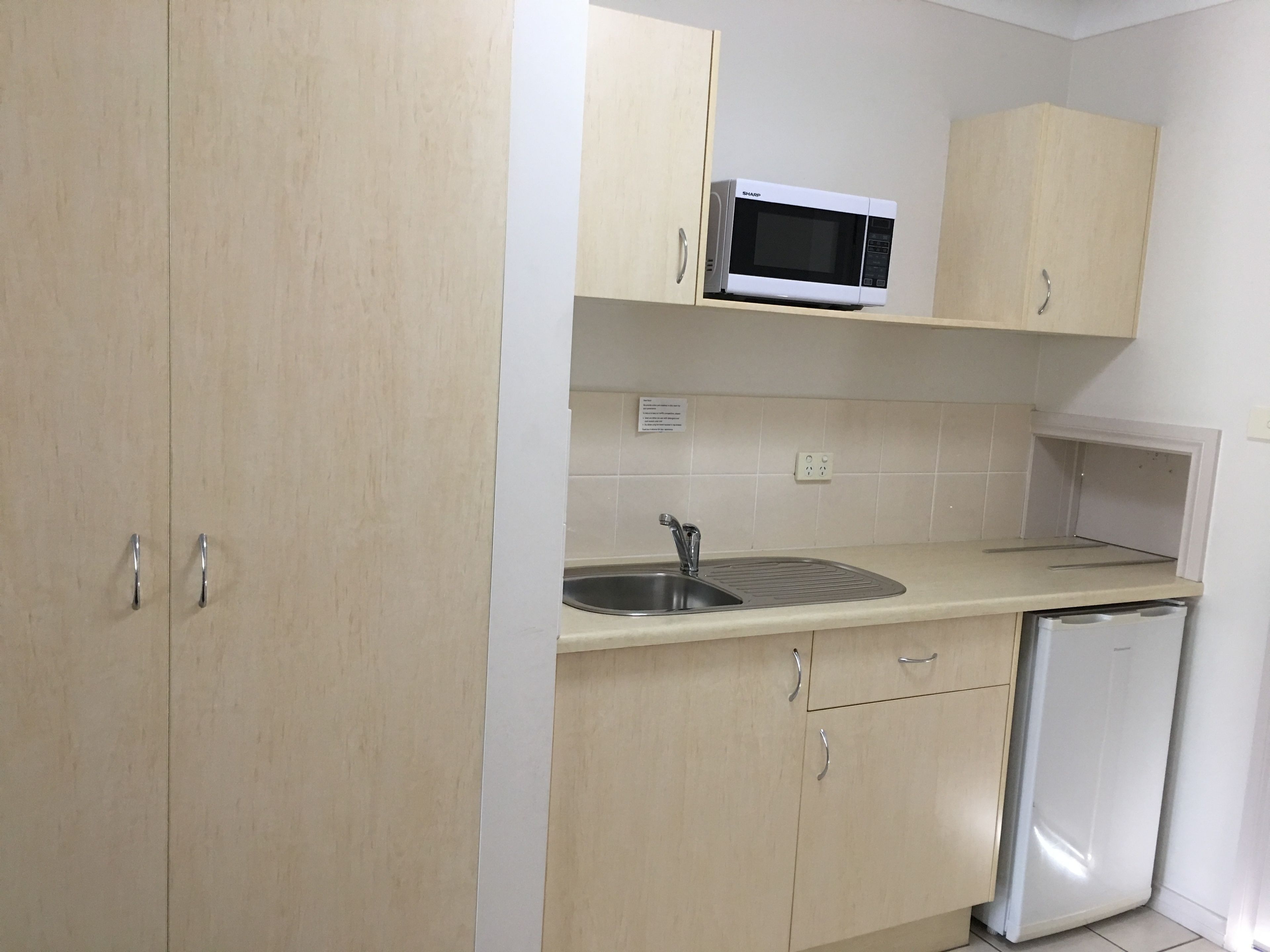 A kitchen with light wooden cabinets, a stainless steel sink, a microwave, and a built-in dishwasher.