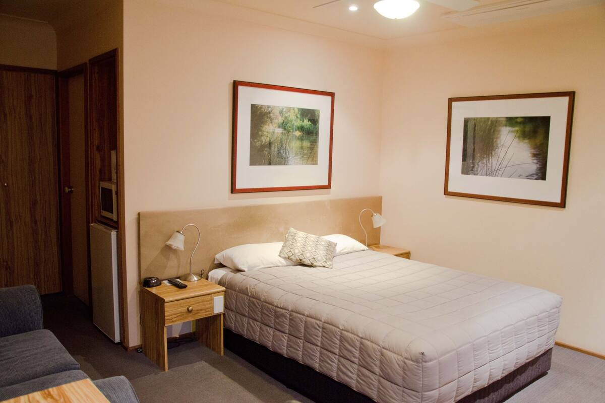 A hotel room with a bed, bedside tables, a desk, a chair, and two framed pictures on the wall.