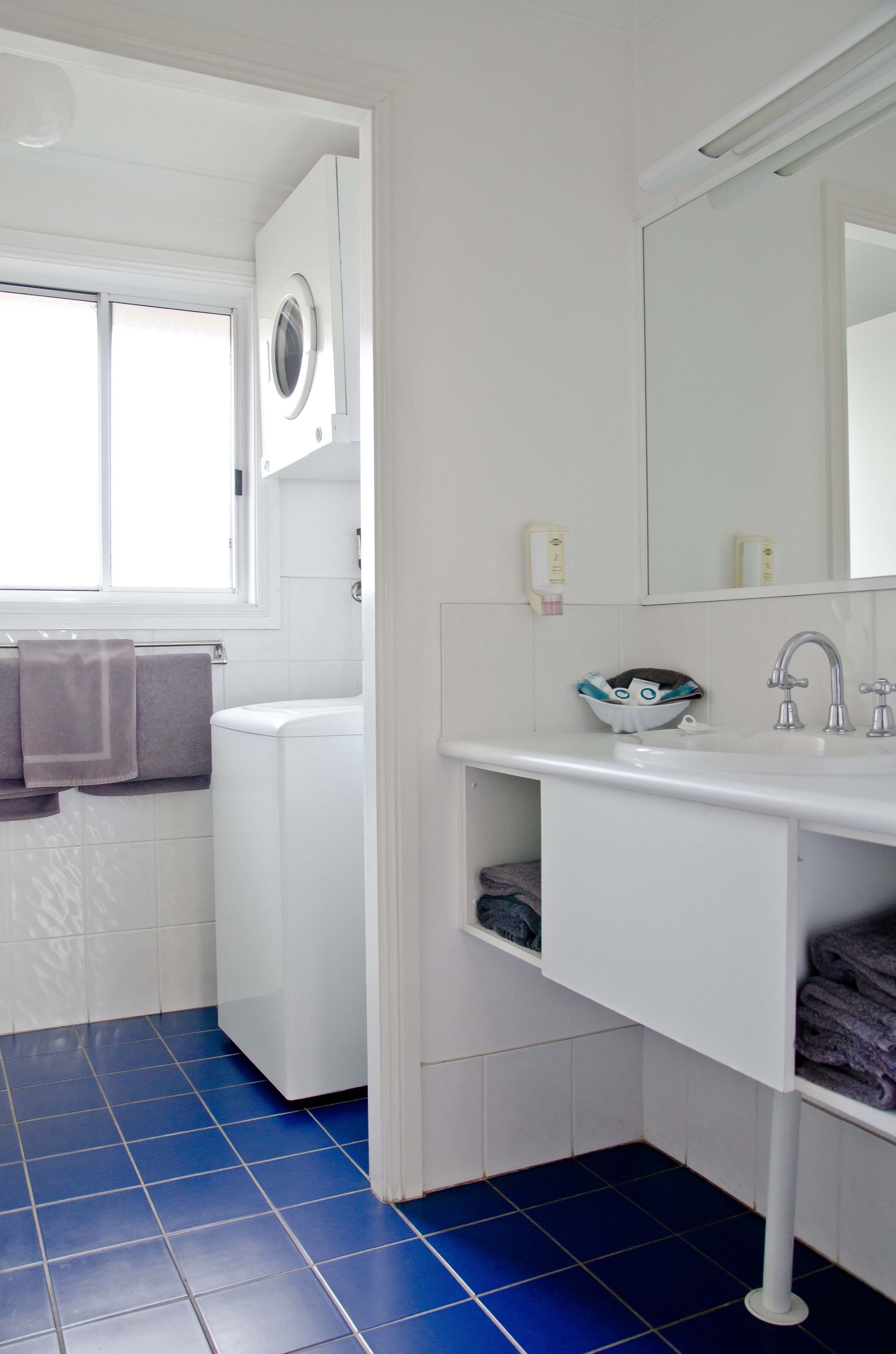 Un baño con lavamanos blanco, espejo, ventana y lavadora.