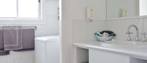 Un baño con lavamanos blanco, espejo, ventana y lavadora.
