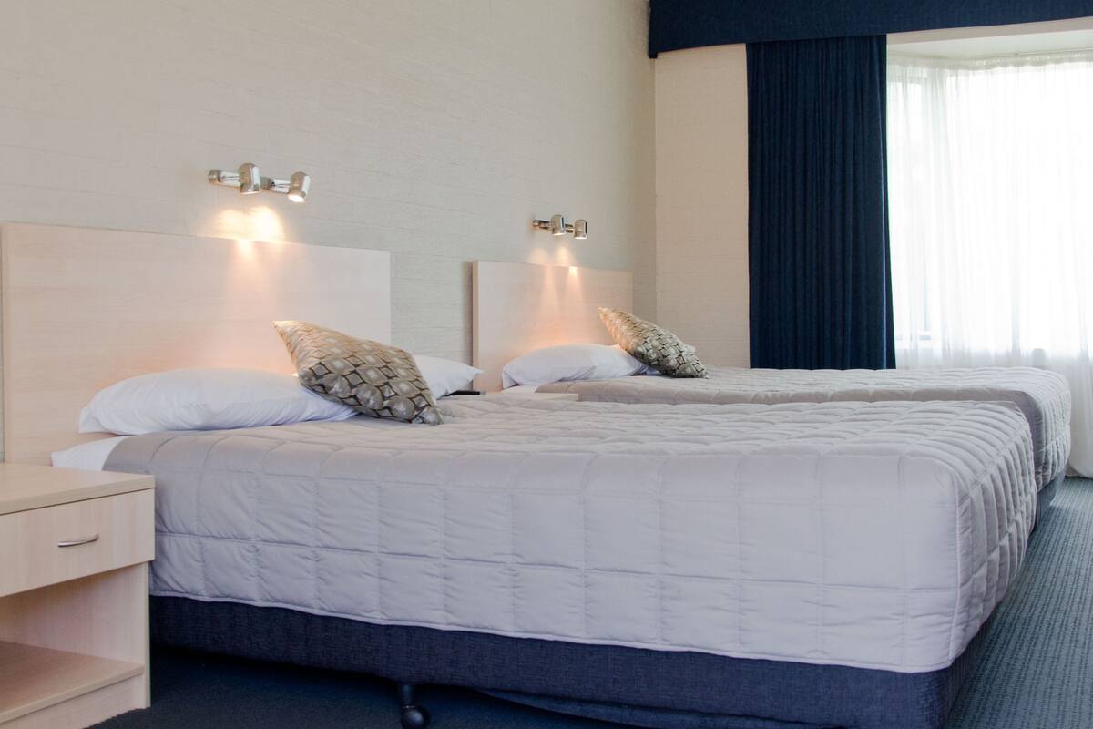 A hotel room with two beds, a ceiling fan, and a window with curtains.