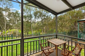 A covered outdoor area with a wooden table and chairs, surrounded by a green fence and trees. - Levi Adelaide Holiday Park (Vale Park)