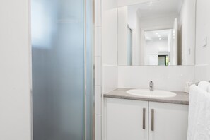 A modern bathroom with a white sink, a mirror, and a shower area. - Levi Adelaide Holiday Park (Vale Park)