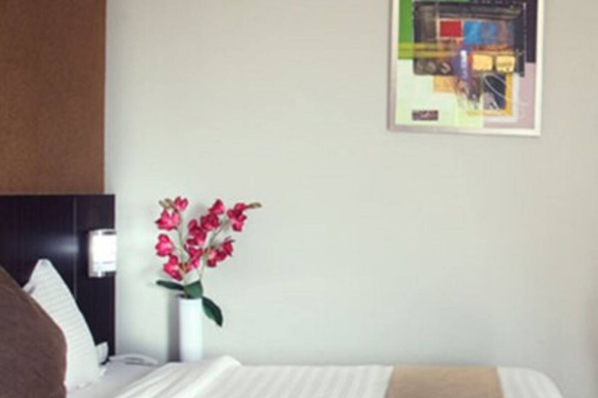 A neatly made bed with a white and beige bedspread, a brown pillow, and a vase with pink flowers on a nightstand.