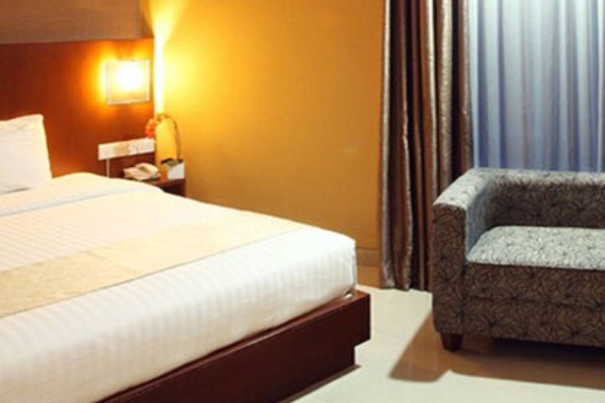 A hotel room with a large bed, a bedside table with a lamp, a chair, and a window with curtains.