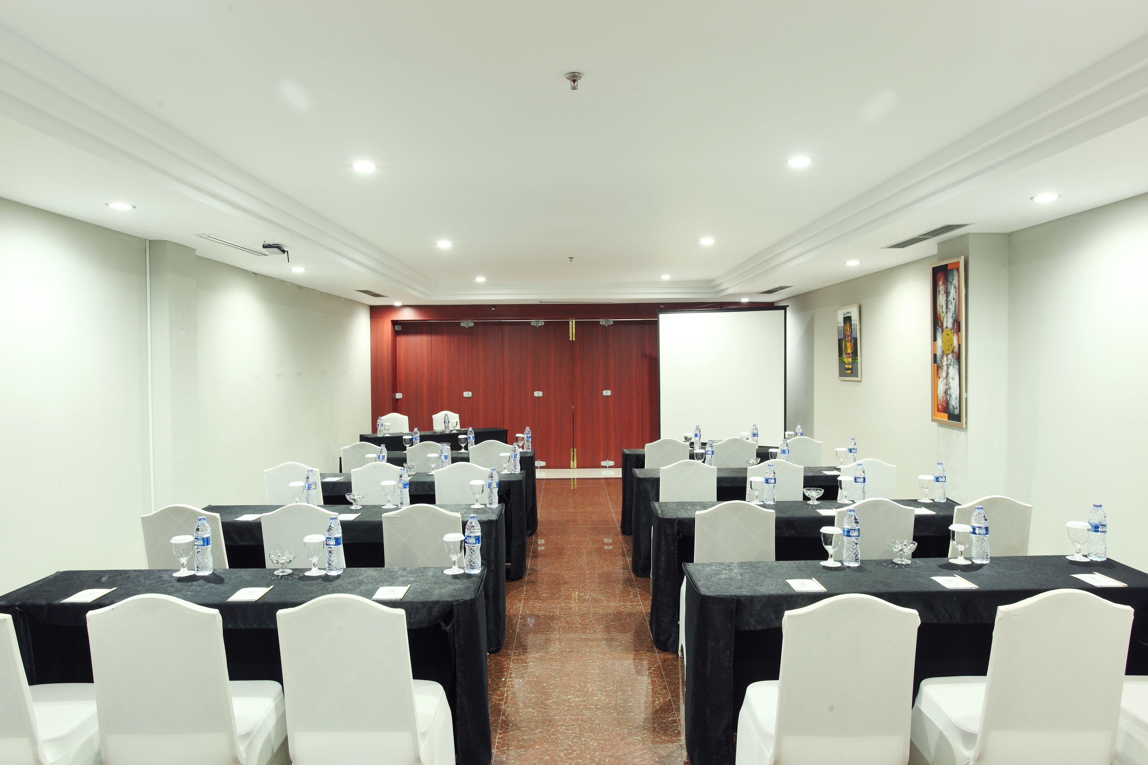 Un salón de conferencias con varias mesas, sillas blancas y botellas de agua.