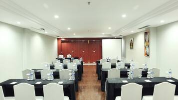 Un salón de conferencias con varias mesas, sillas blancas y botellas de agua.