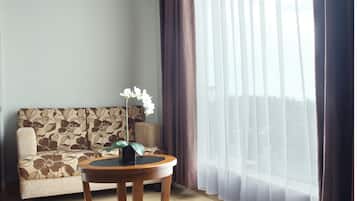 Una sala de estar con un sofá, una mesa redonda de madera con un florero y cortinas translúcidas.
