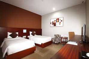 Two single beds with white linens and brown pillows, a wooden headboard, and a flat-screen television.