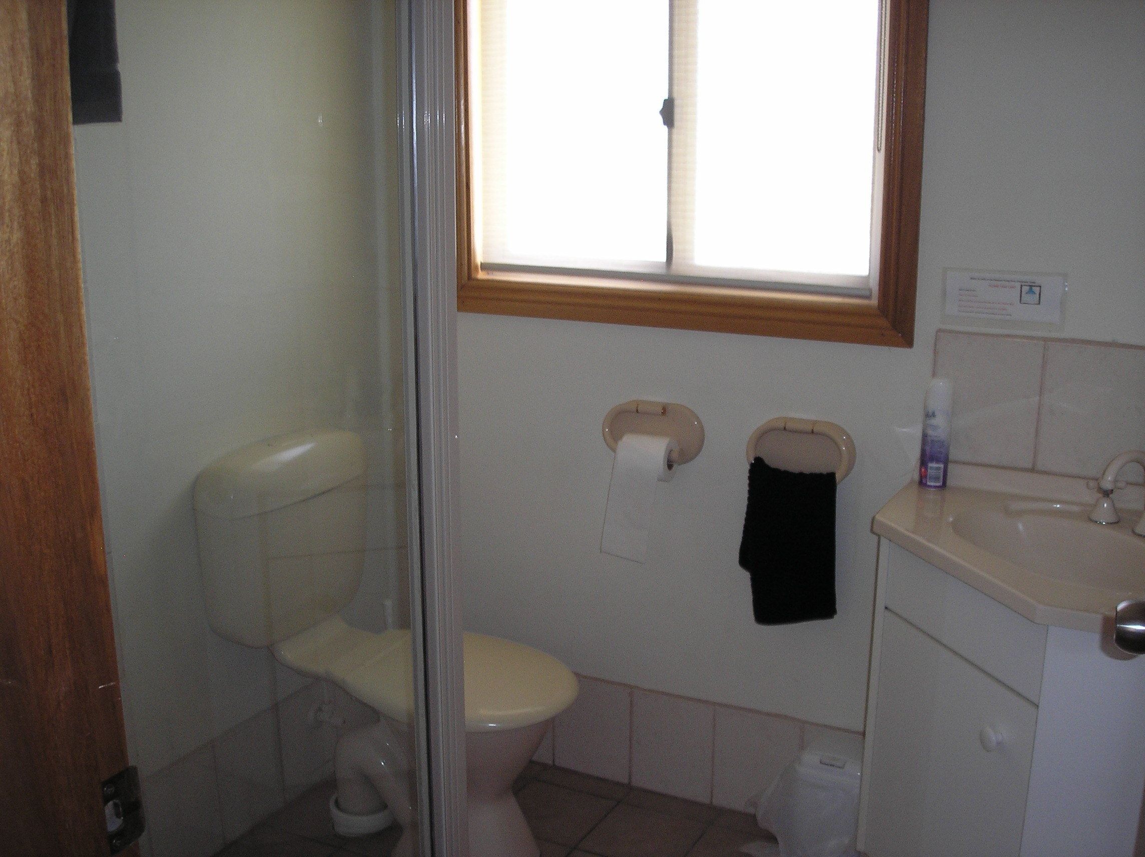 Et badeværelse med toilet, bruser, vask og et vindue.