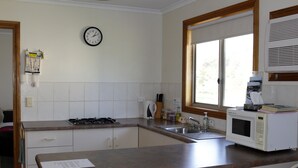 A kitchen with a stove, sink, microwave, and a clock on the wall. - Cape Jervis Holiday Units (Cape Jervis)