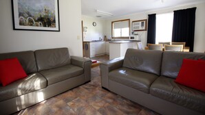 A living room with two leather sofas, a coffee table, and a dining area with a table and chairs. - Cape Jervis Holiday Units (Cape Jervis)