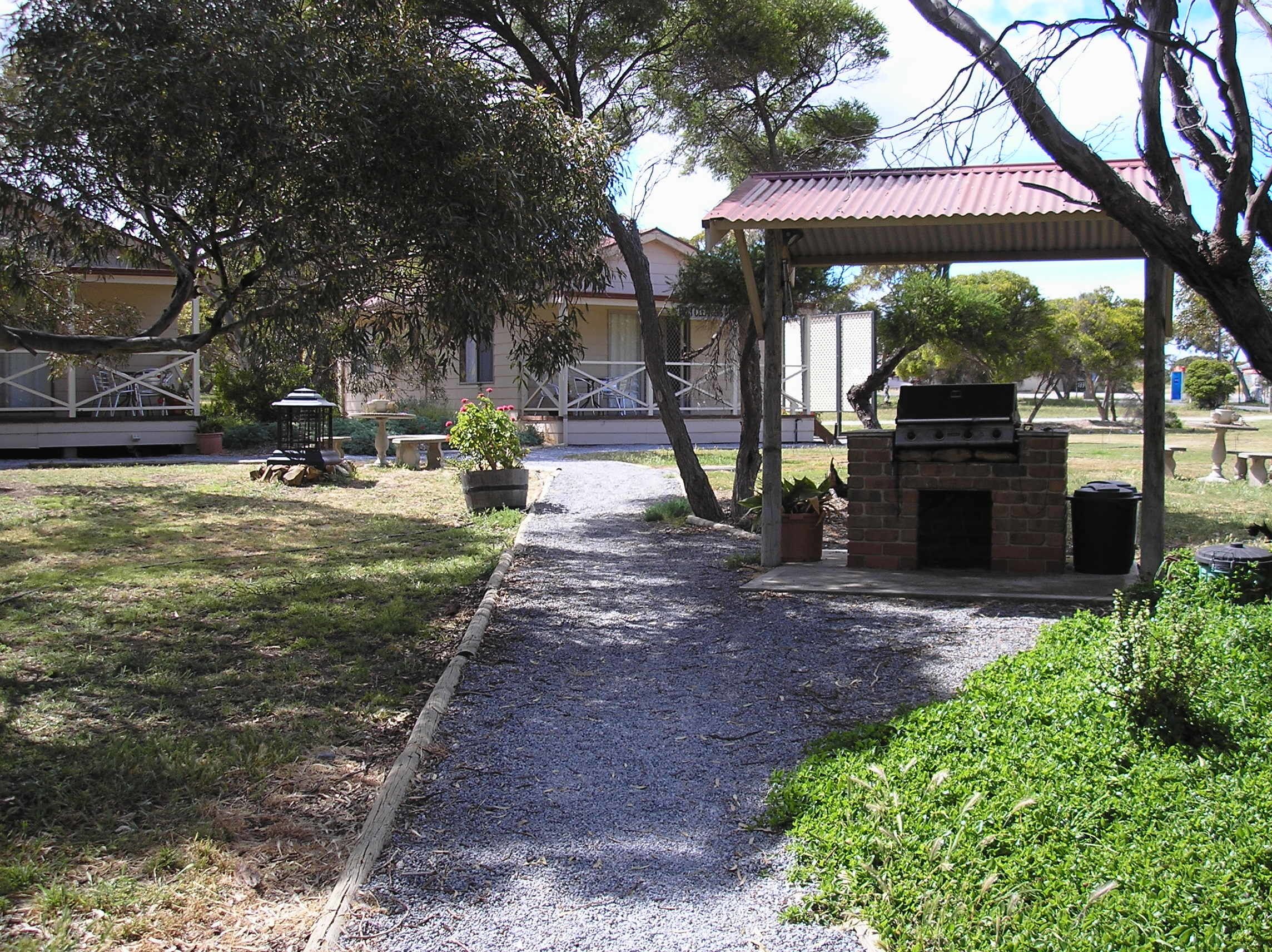 A covered outdoor area with a barbecue grill, a pathway, and a building in the background.