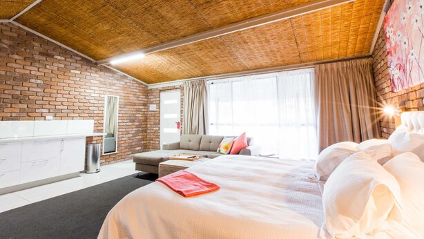 Una habitación de hotel moderna con pared de ladrillo, una cama grande con ropa blanca, un sofá y un área de comedor.