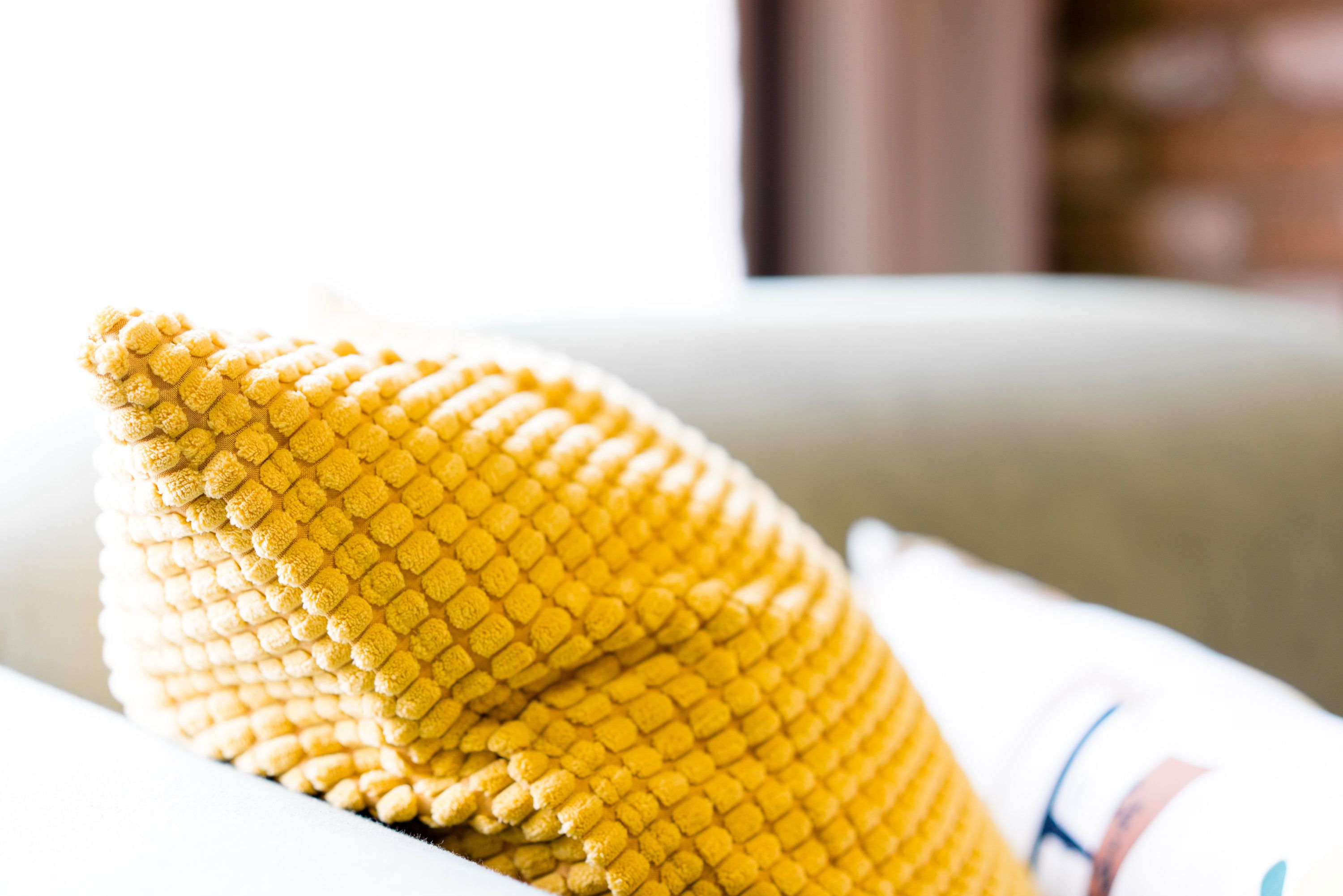 Un cojín amarillo con textura sobre un sofá blanco.