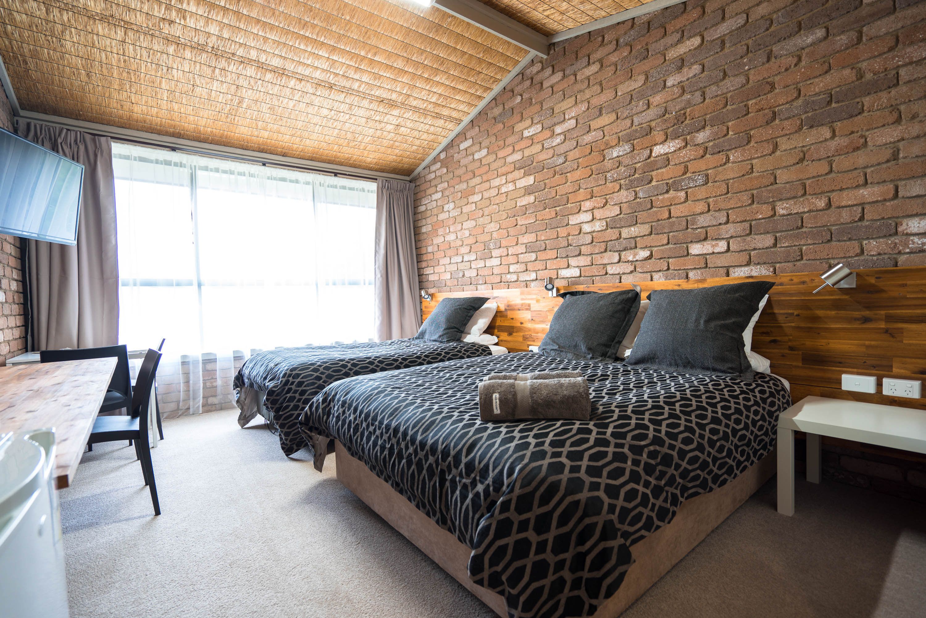 A room with two beds, a wooden desk, and a brick wall.