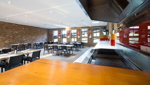 Un comedor espacioso con paredes de ladrillo, ventanas amplias y un piano en el centro. Mesas y sillas dispuestas para comer.