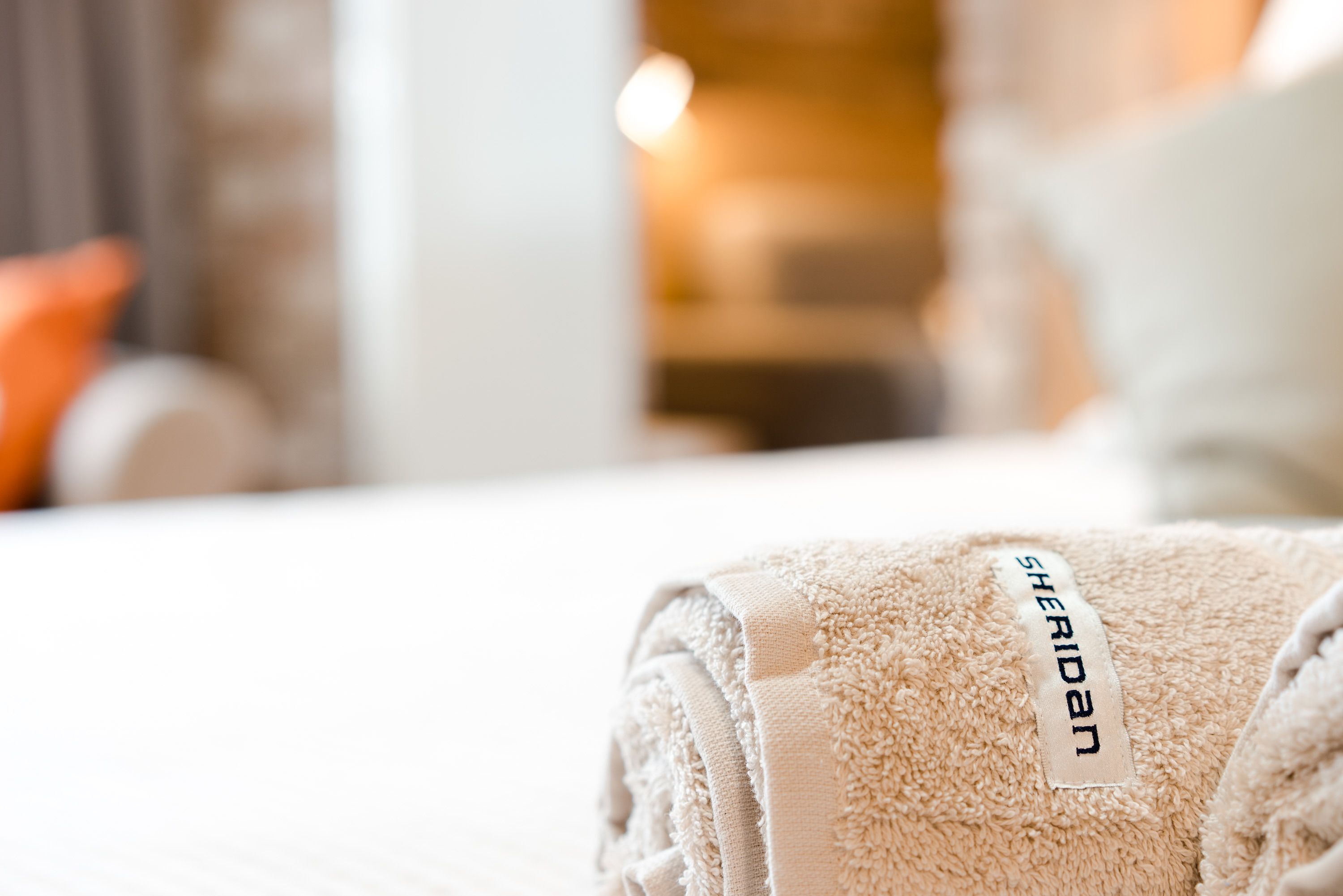 A neatly folded beige towel with a 'Sheridan' tag on a bed.