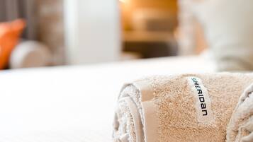 A neatly folded beige towel with a 'Sheridan' tag on a bed.