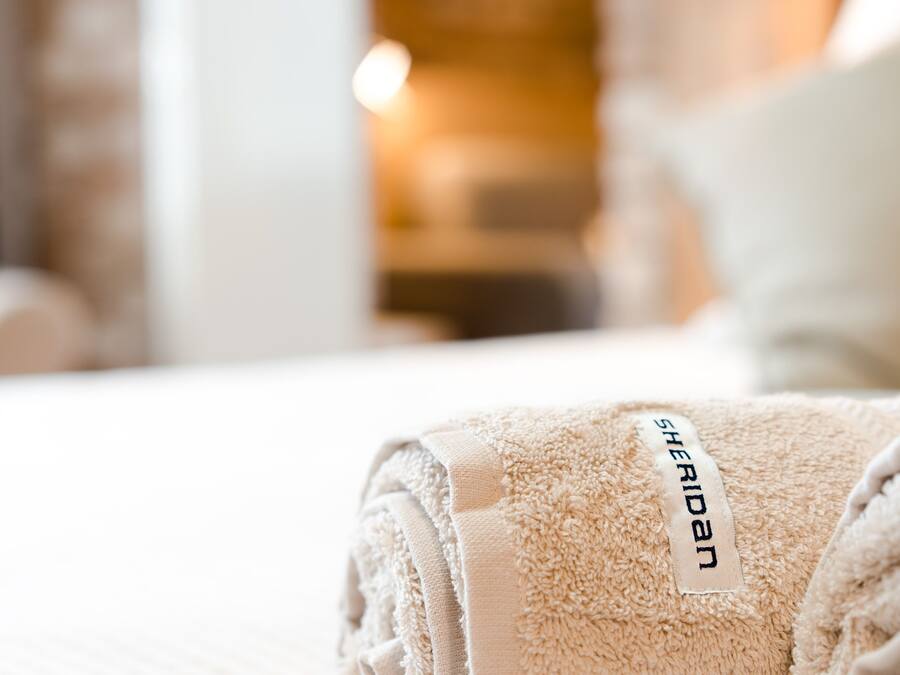 A neatly folded beige towel with a 'Sheridan' tag on a bed.