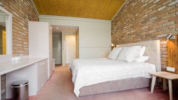 A bedroom with a brick wall, a bed with white bedding, a bedside table, and a small trash bin.