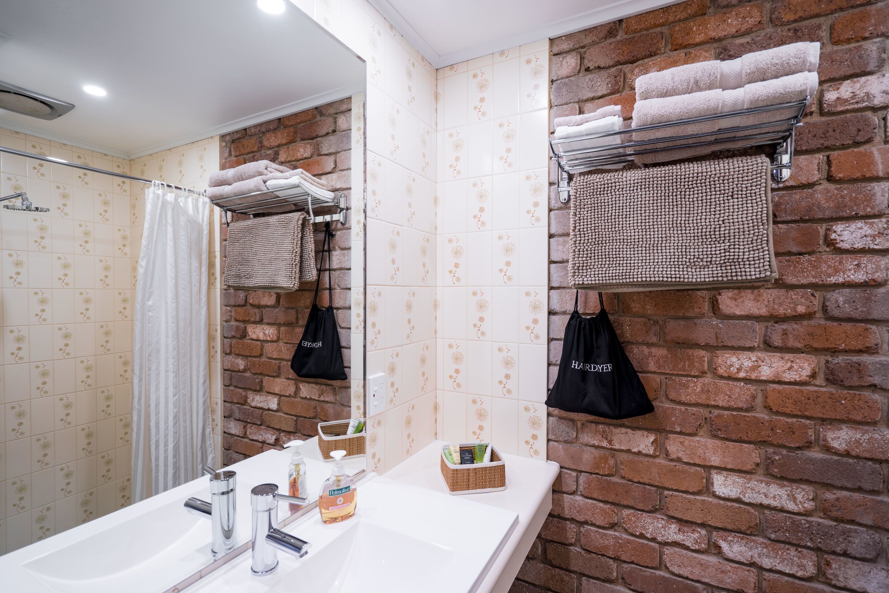 A bathroom with a white sink, mirror, and a shower area. There are towels and toiletries on the counter.