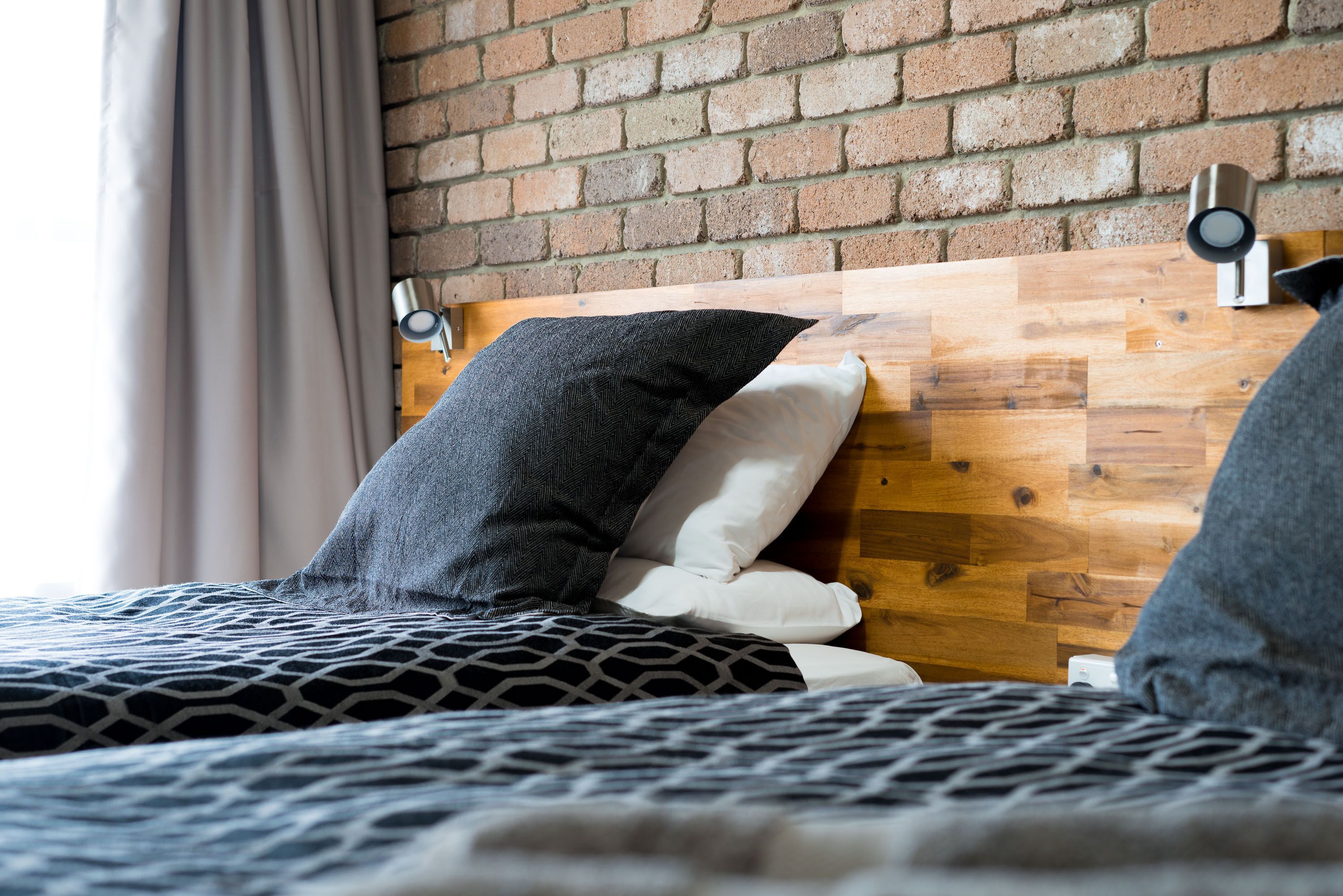 A bed with a wooden headboard, a patterned bedspread, and two pillows.
