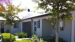 A modern building with a flat roof, a garage door, and a small garden area with various plants and shrubs. - Darfield Motel (Darfield)