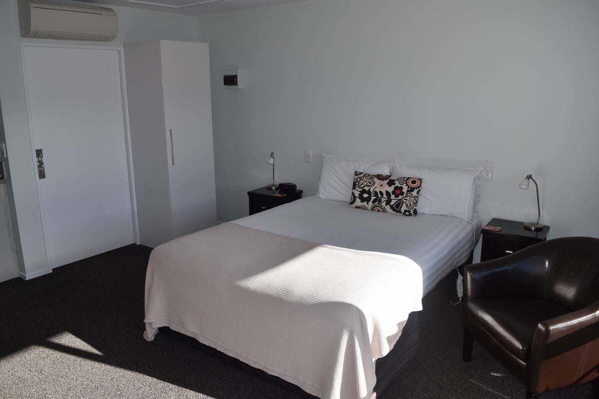 Una habitación de hotel con cama, mesita de noche, silla y armario.